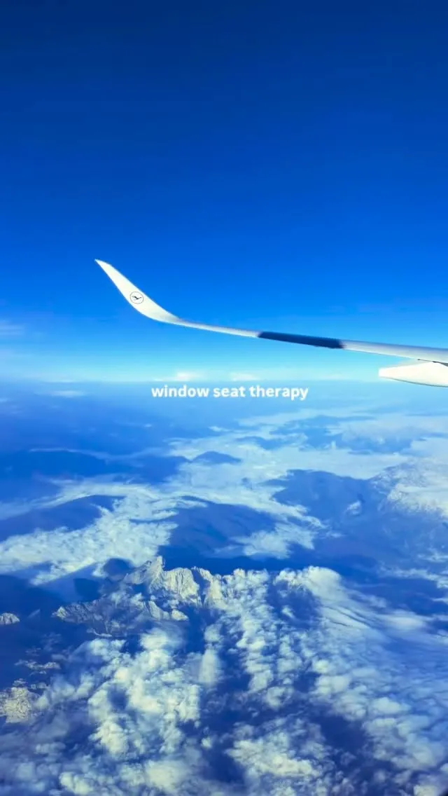 The view from an aeroplane window, a wing above snow-dusted mountains and clouds under a deep blue sky.